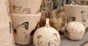 Cracked-effect ceramic pots and balls with butterfly print. 2 carved wooden chickens in the background