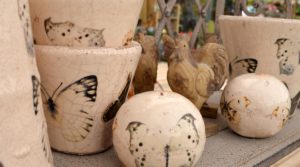 Cracked-effect ceramic pots and balls with butterfly print. Wooden chickens in background